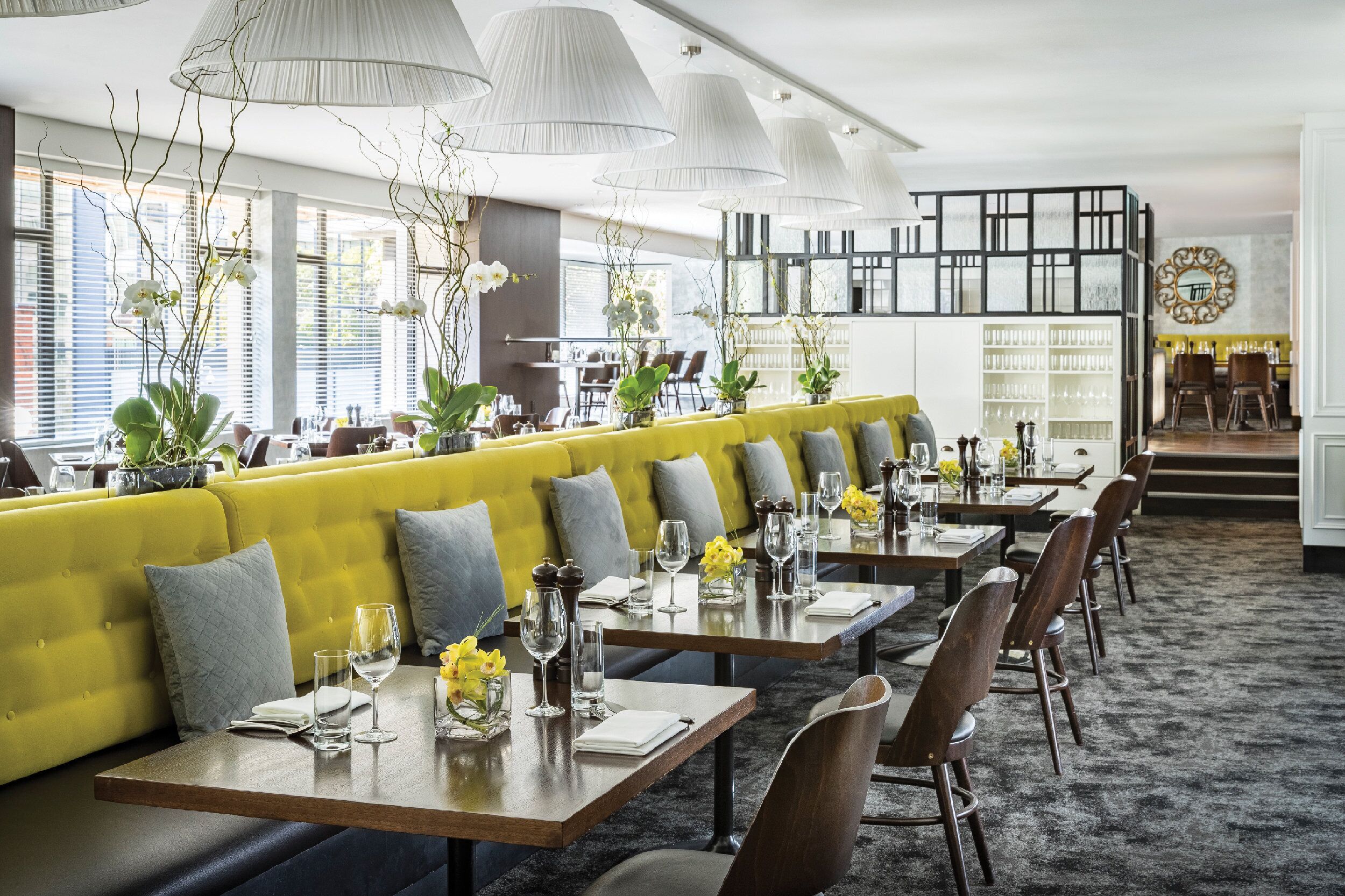 A restaurant with yellow seating, wooden tables, and hanging lamps.