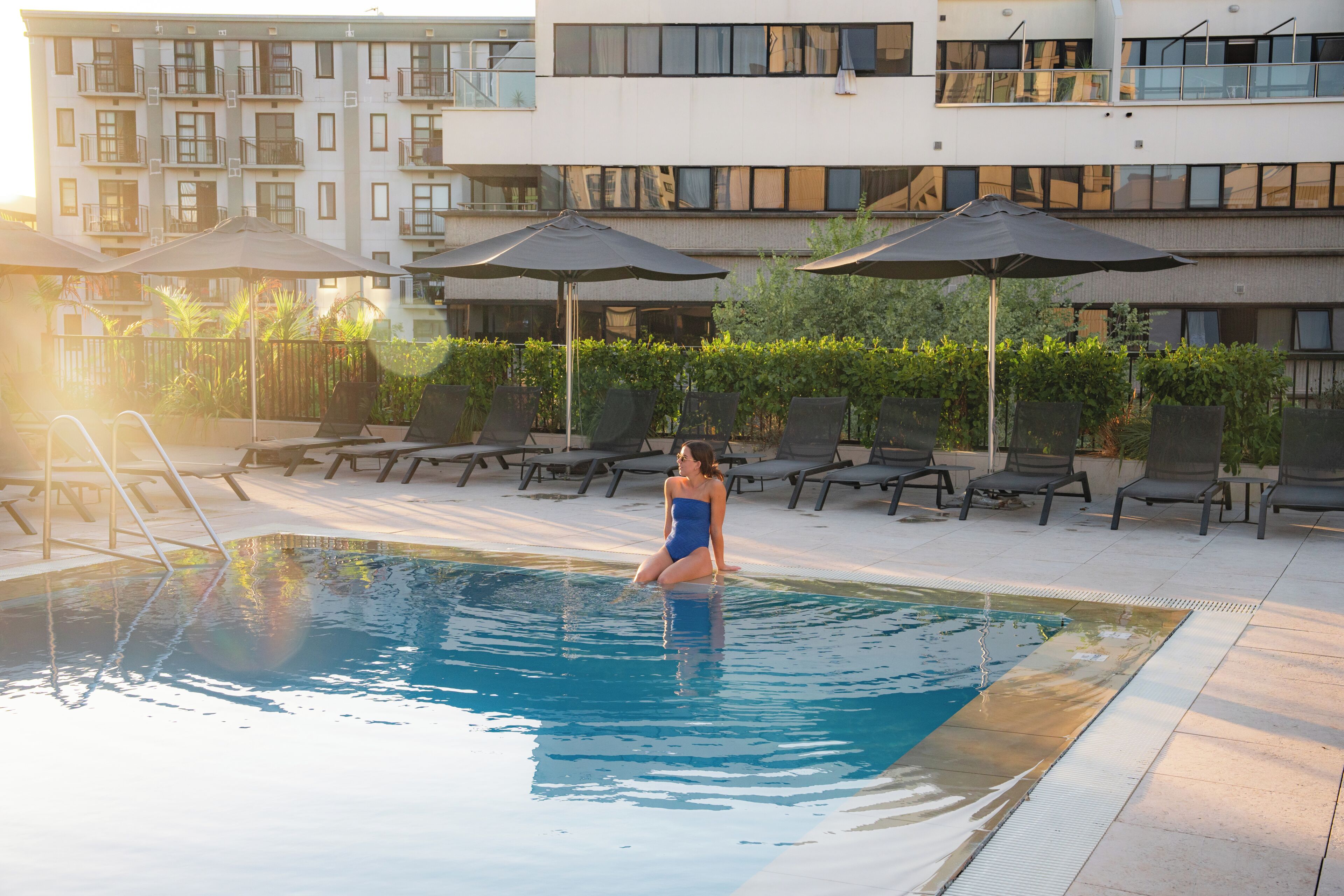 A swimming pool with lounge chairs and umbrellas, surrounded by a building with multiple balconies.
