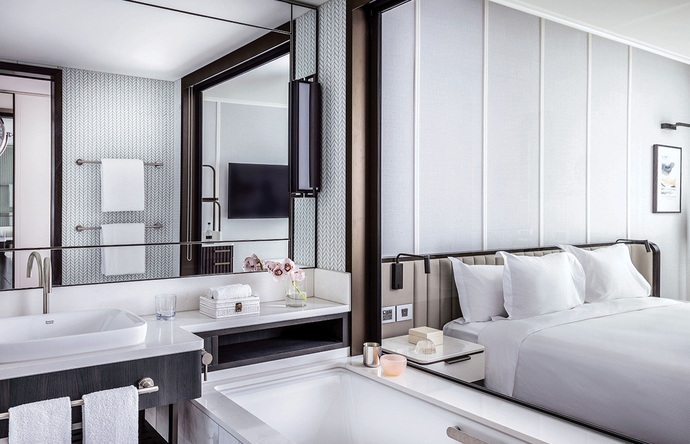 A modern hotel room with a large bed, a separate bathroom with a sink, and a mirror.