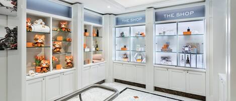 Un hall de hotel con vitrinas de vidrio con la etiqueta "THE SHOP", suelo de mármol y una barandilla de metal.