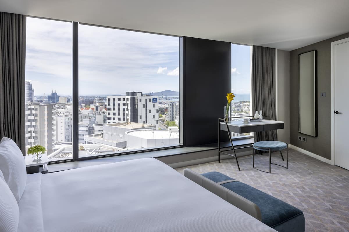 A modern hotel room with a large bed, a desk, and a view of the cityscape.
