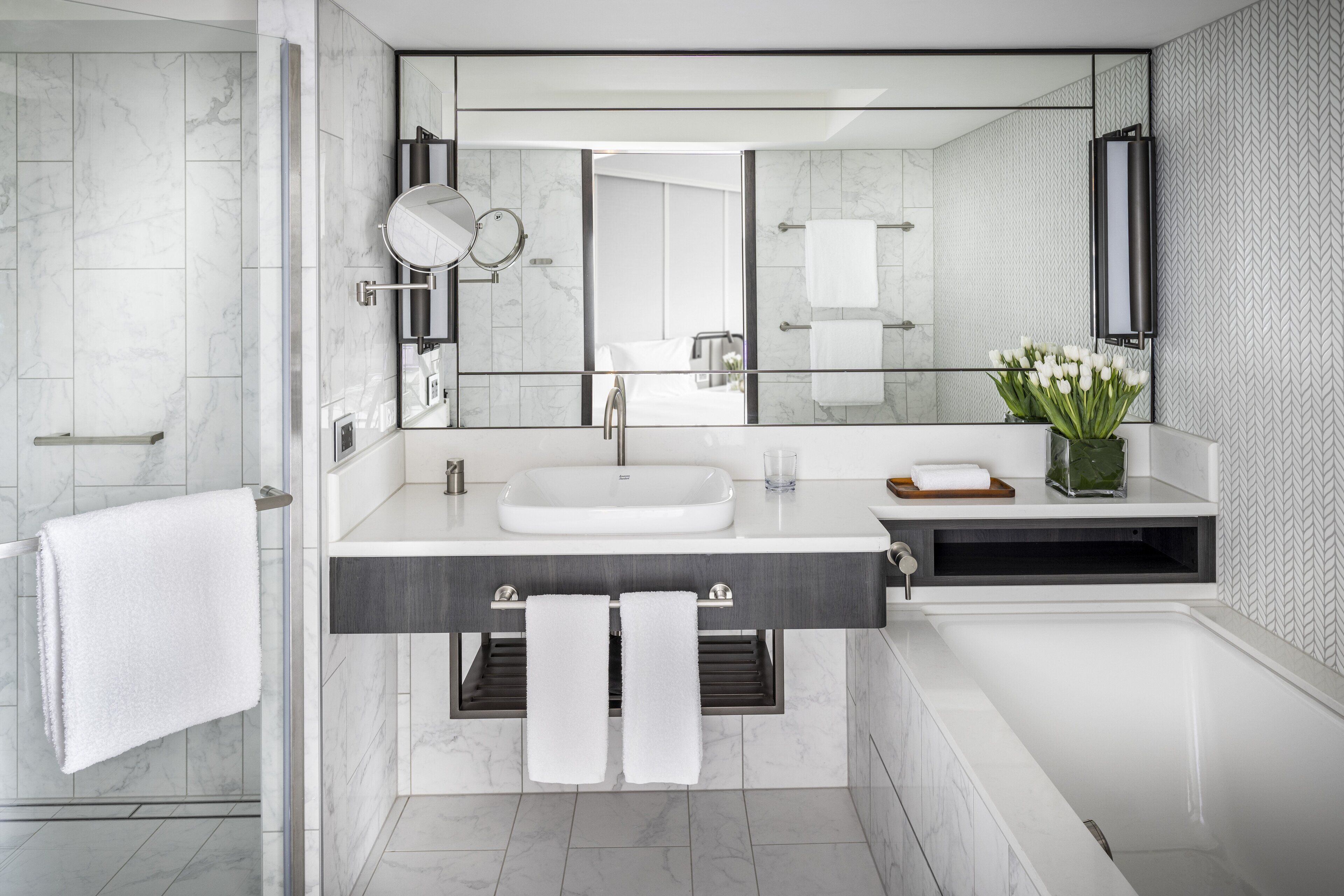 A modern bathroom with a large mirror, white sink, and a glass shower enclosure.