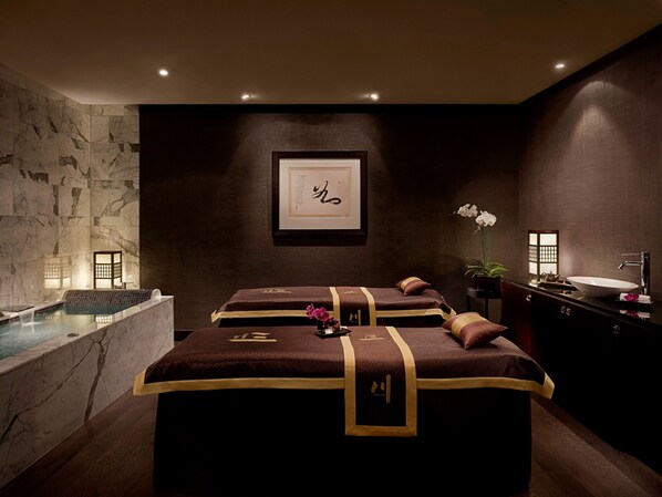 A spa room with a marble wall, a framed artwork, a massage table, a bathtub, and a sink.