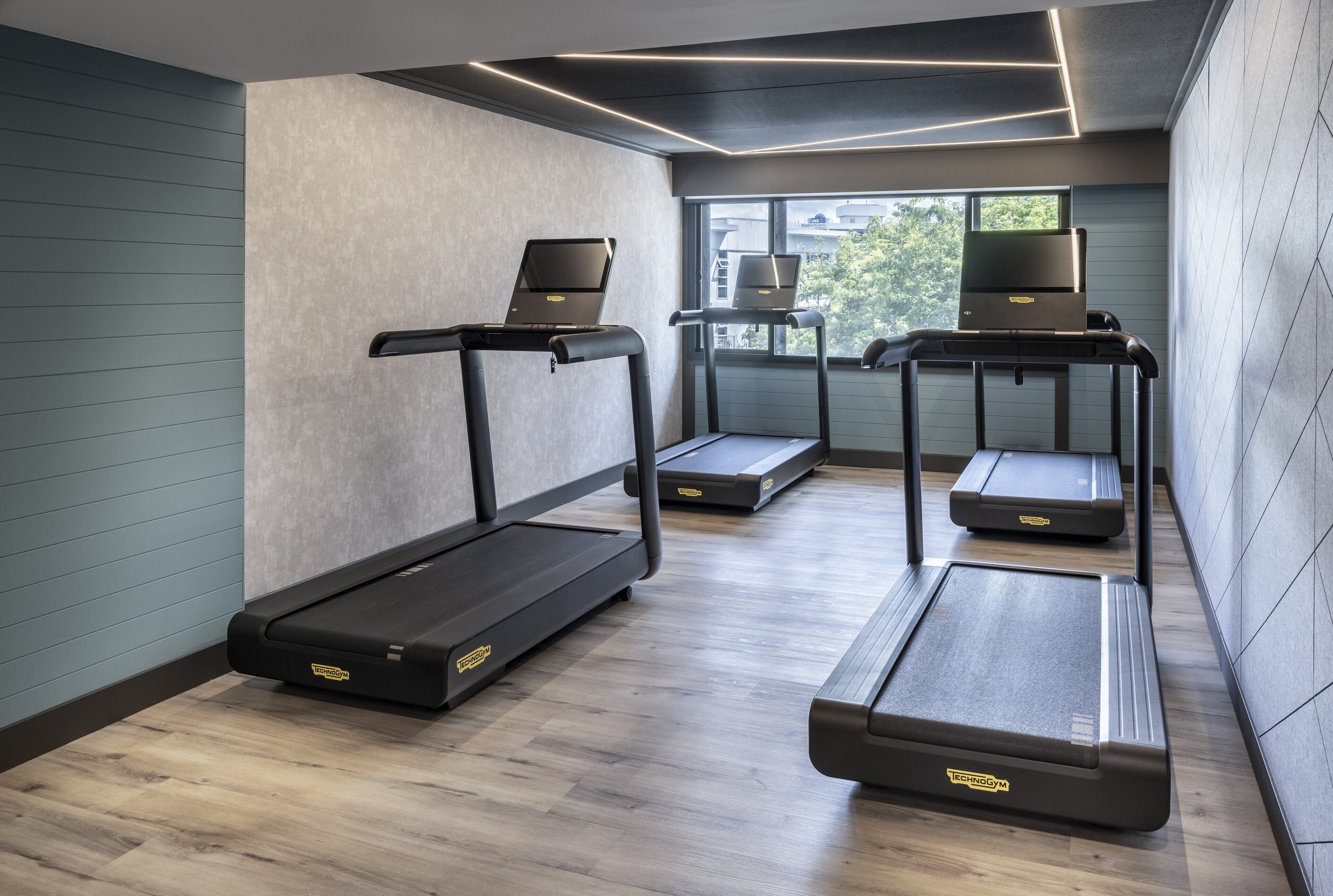 Un gimnasio moderno con tres cintas de correr, cada una con un ordenador portátil encima.