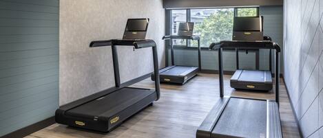 A modern gym with three treadmills, each with a laptop on top.