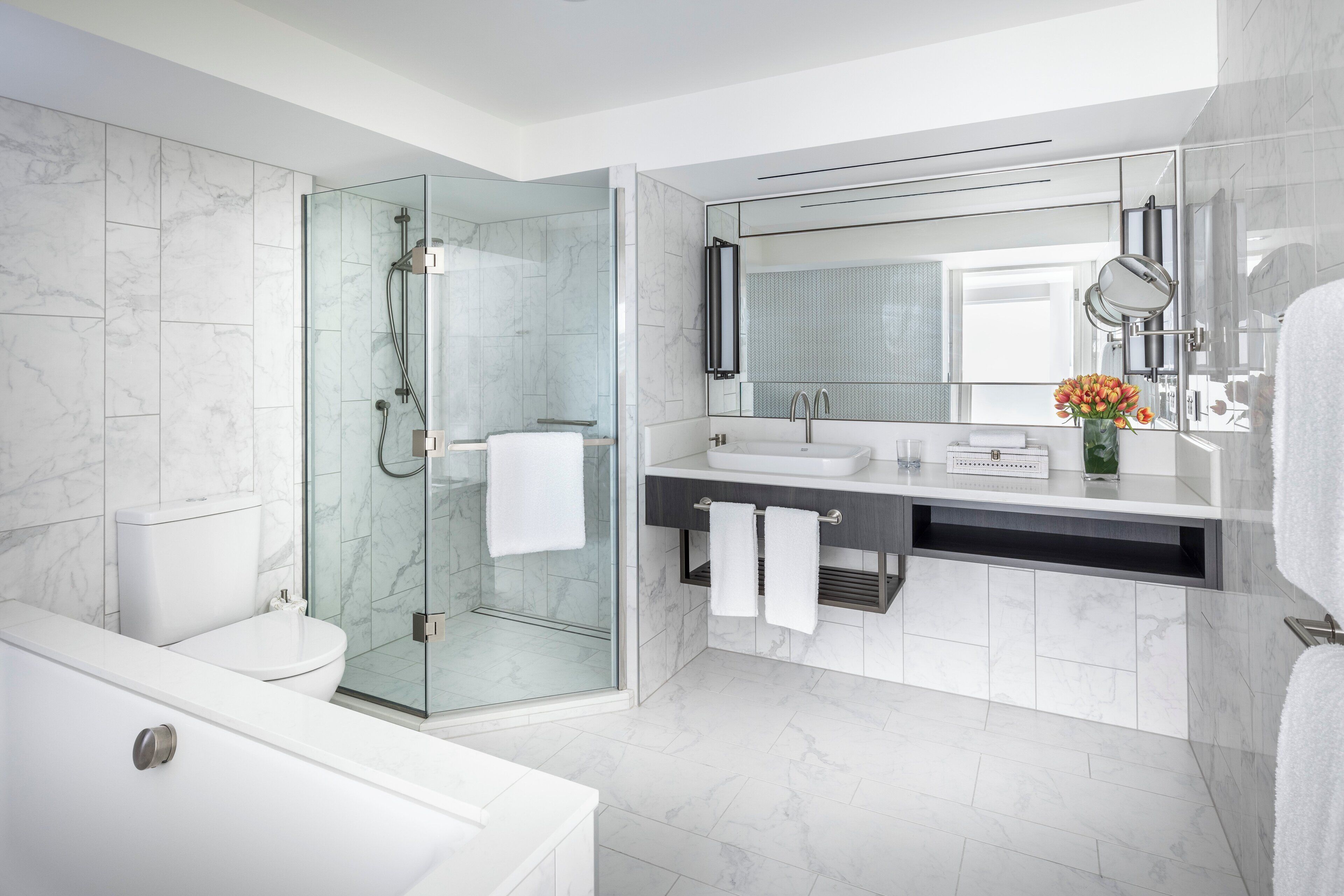A modern bathroom with a glass-enclosed shower, a white toilet, a bathtub, and a vanity with a mirror.