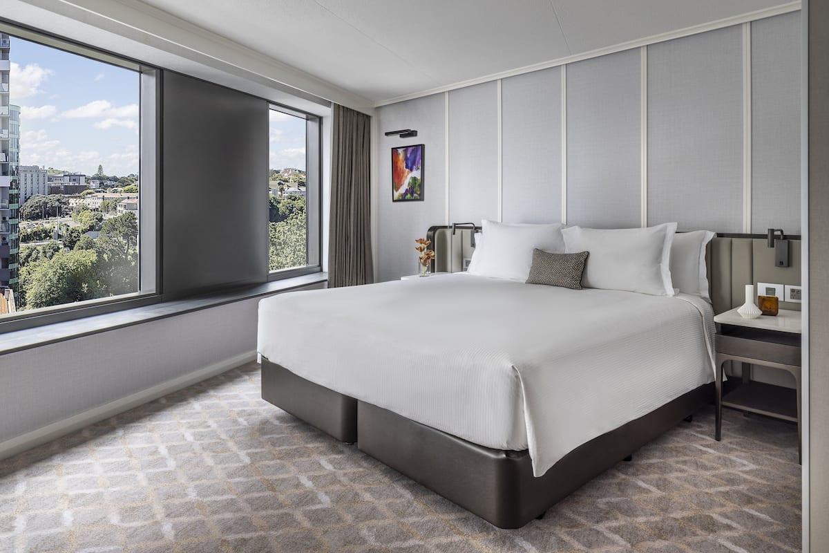 A modern hotel room with a large bed, a bedside table, and a view of the city.