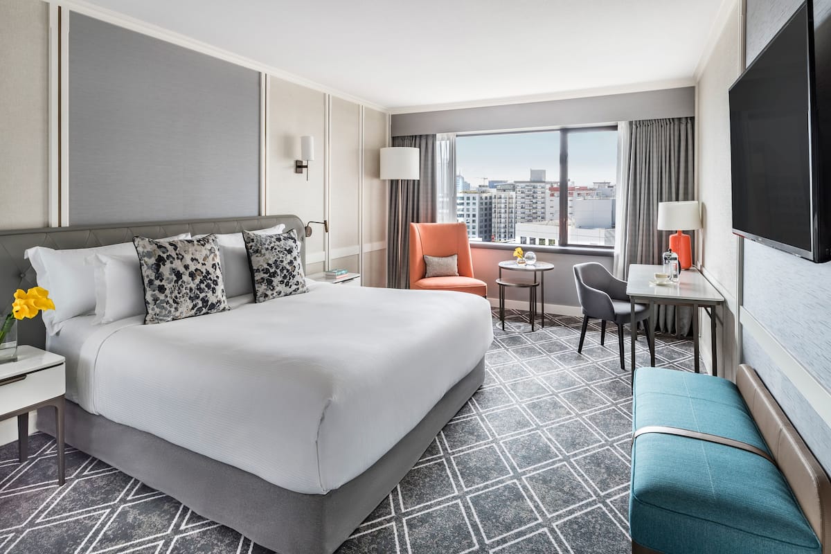 A hotel room with a large bed, a desk, a chair, and a TV.