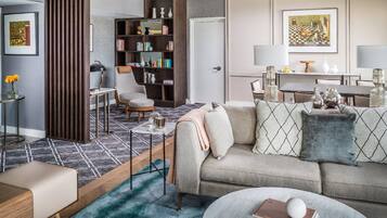 Una sala de estar con sofá, sillón y mesa de centro. Hay una estantería y un comedor con mesa y sillas.