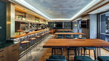 Un área de bar moderna con una barra alargada, taburetes y un mural en el techo.