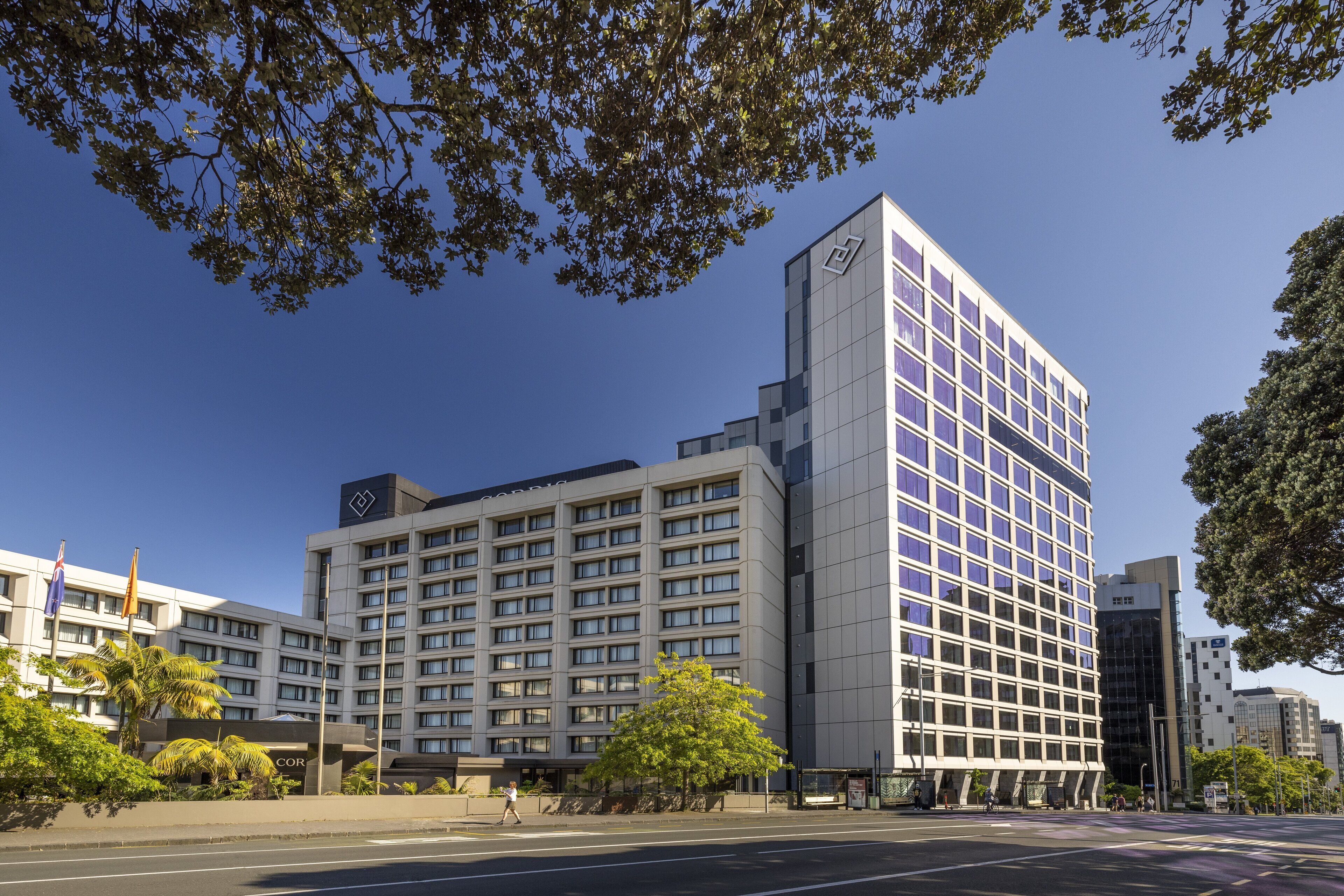 Un hôtel moderne, situé dans un immeuble imposant à l’angle d’une rue, doté de grandes fenêtres et d’un logo bien visible.