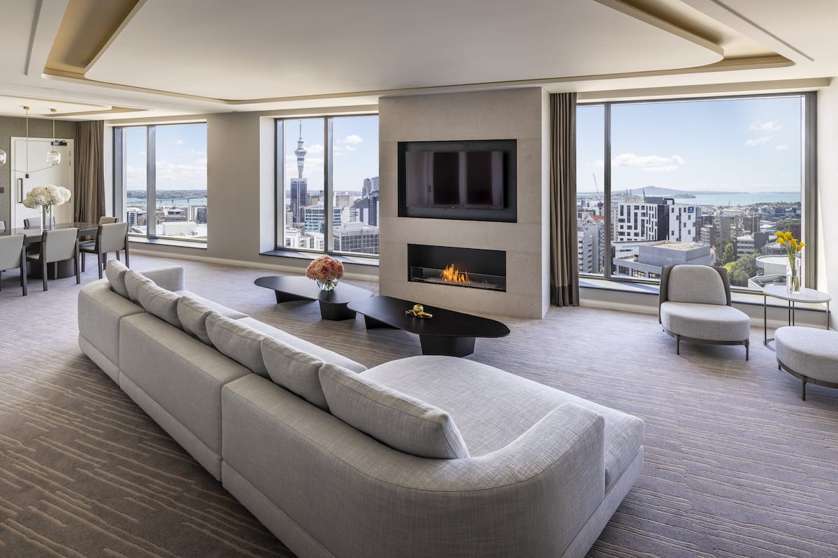 A modern living room with a large sofa, a fireplace, a TV, and a city view.