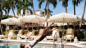 A swimming pool with lounge chairs and umbrellas, surrounded by palm trees and a building in the background. - The Colony Hotel Palm Beach (Palm Beach)