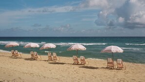 A beach with rows of wooden beach chairs and pink umbrellas.