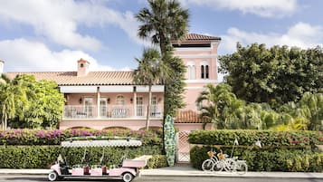 Um edifício rosa com telhado de azulejos, uma palmeira e um carrinho de golfe.