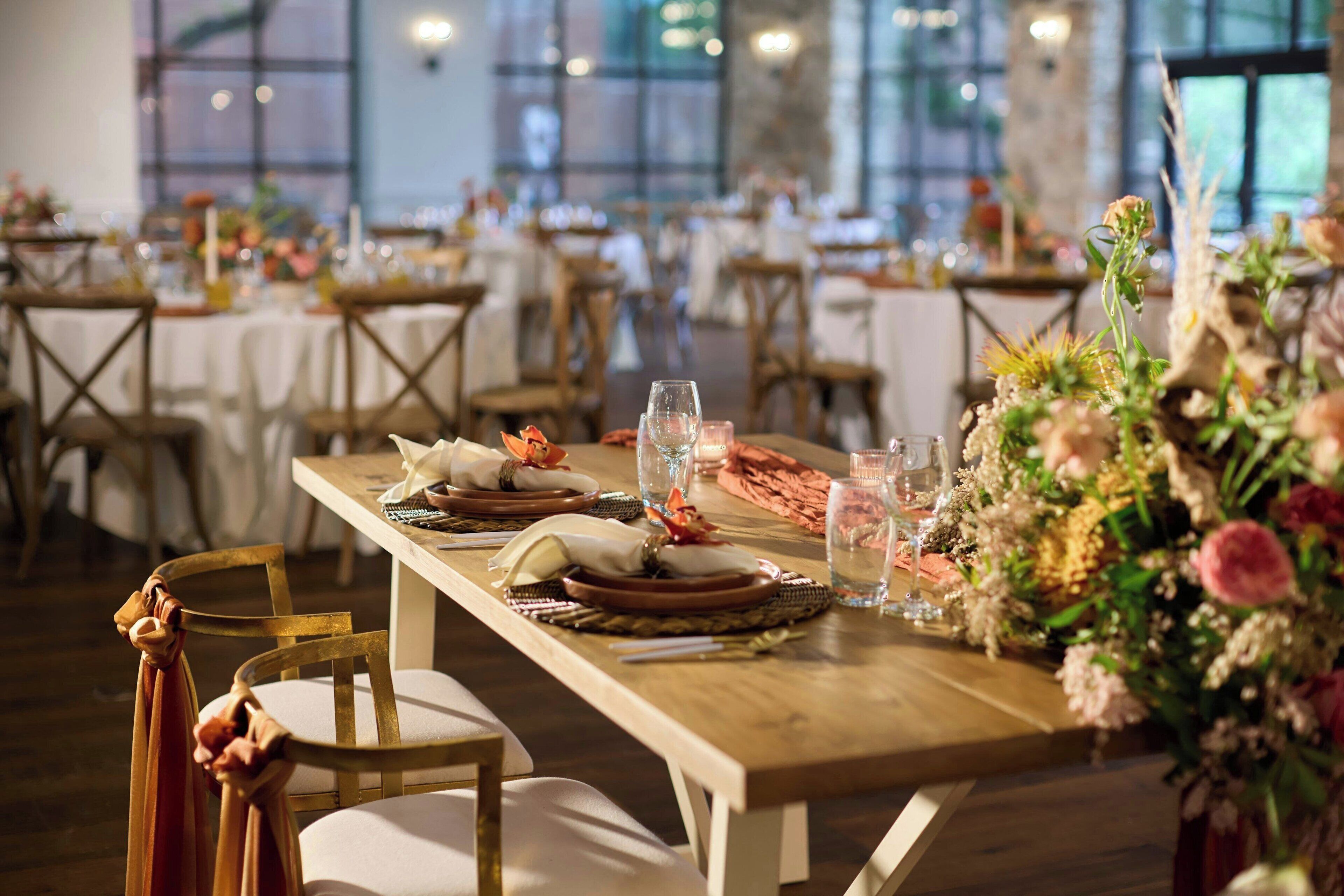 A dining area with wooden tables set for a meal, chairs, and a floral centerpiece.