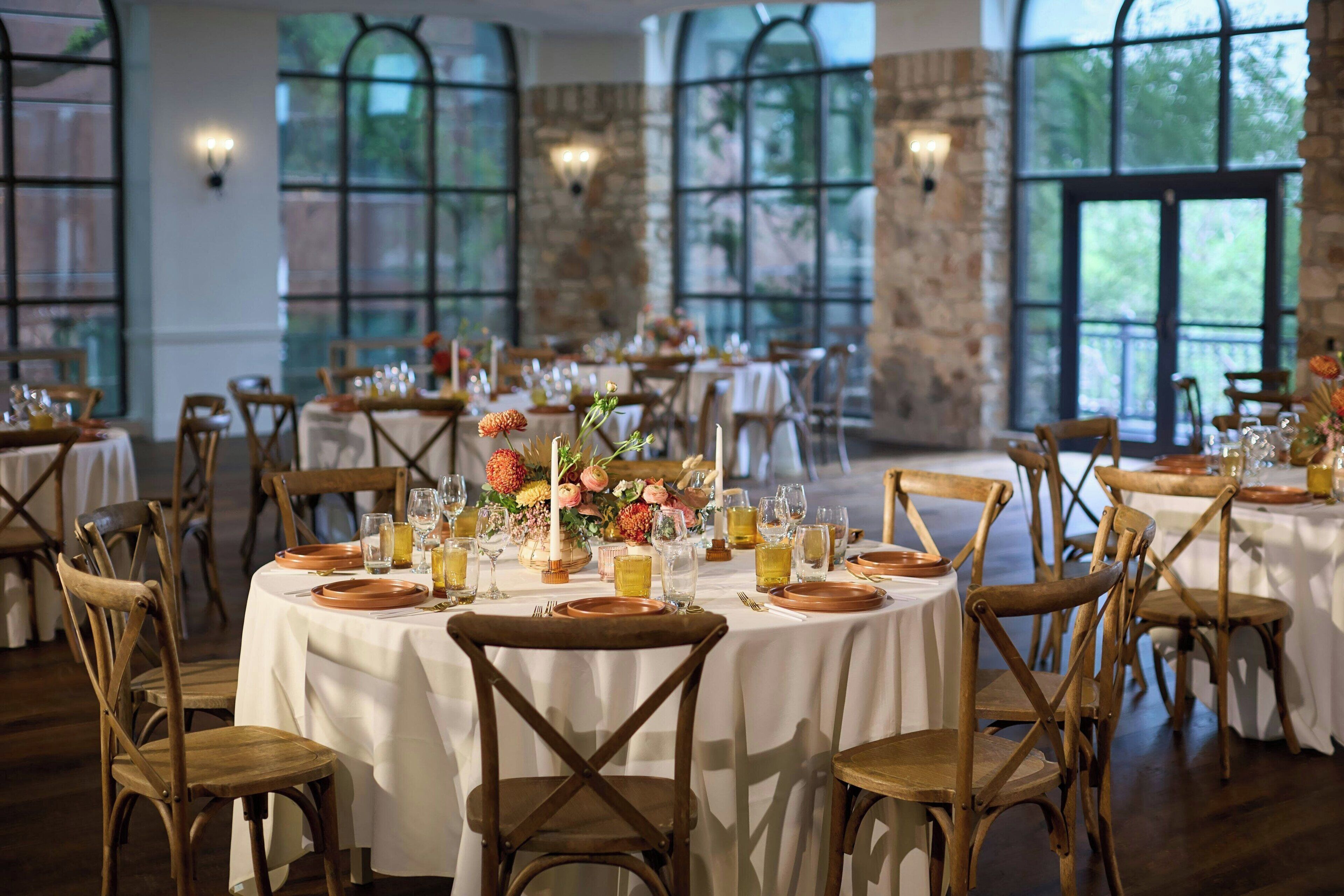 Un comedor con mesas redondas dispuestas para una comida, sillas de madera y ventanas amplias con vista a zonas verdes.