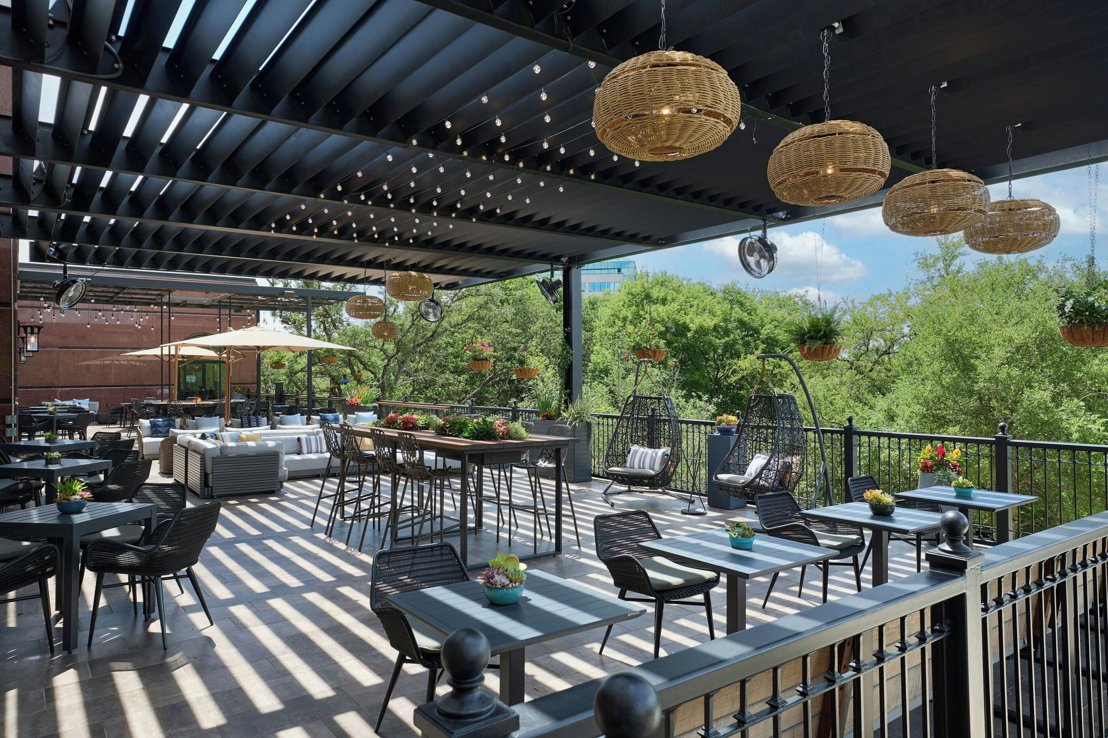 An outdoor patio with tables and chairs, hanging wicker lights, and potted plants.