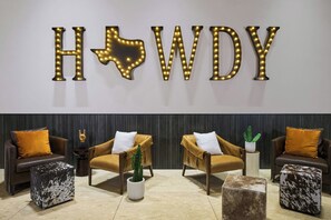 A lobby with a 'HOWDY' sign, leather armchairs, and a cactus plant.