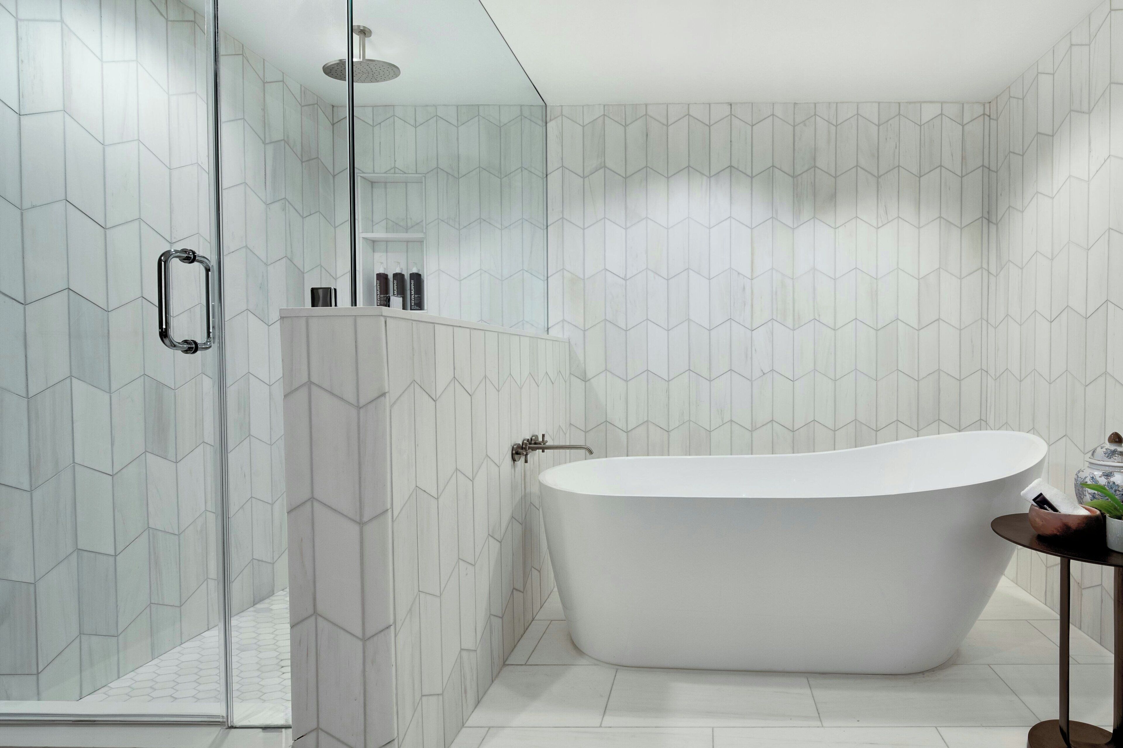 Une salle de bain moderne avec une baignoire sur pieds, une douche à parois de verre et un mur recouvert de carreaux blancs formant un motif géométrique.