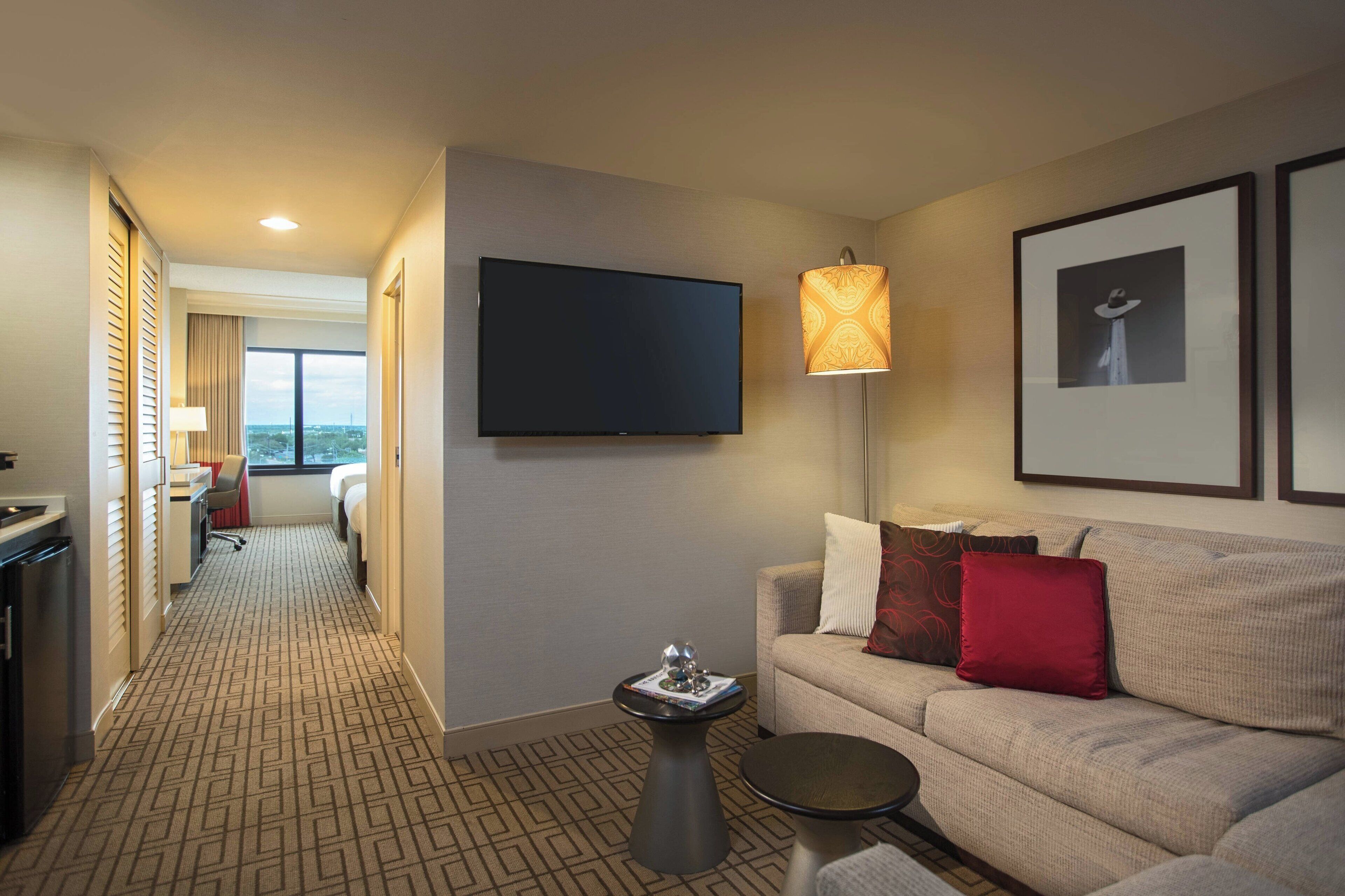 A hotel room with a sofa, a TV, a lamp, and framed pictures on the wall.
