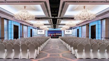 A conference room with rows of chairs, a large screen at the front, and chandeliers.