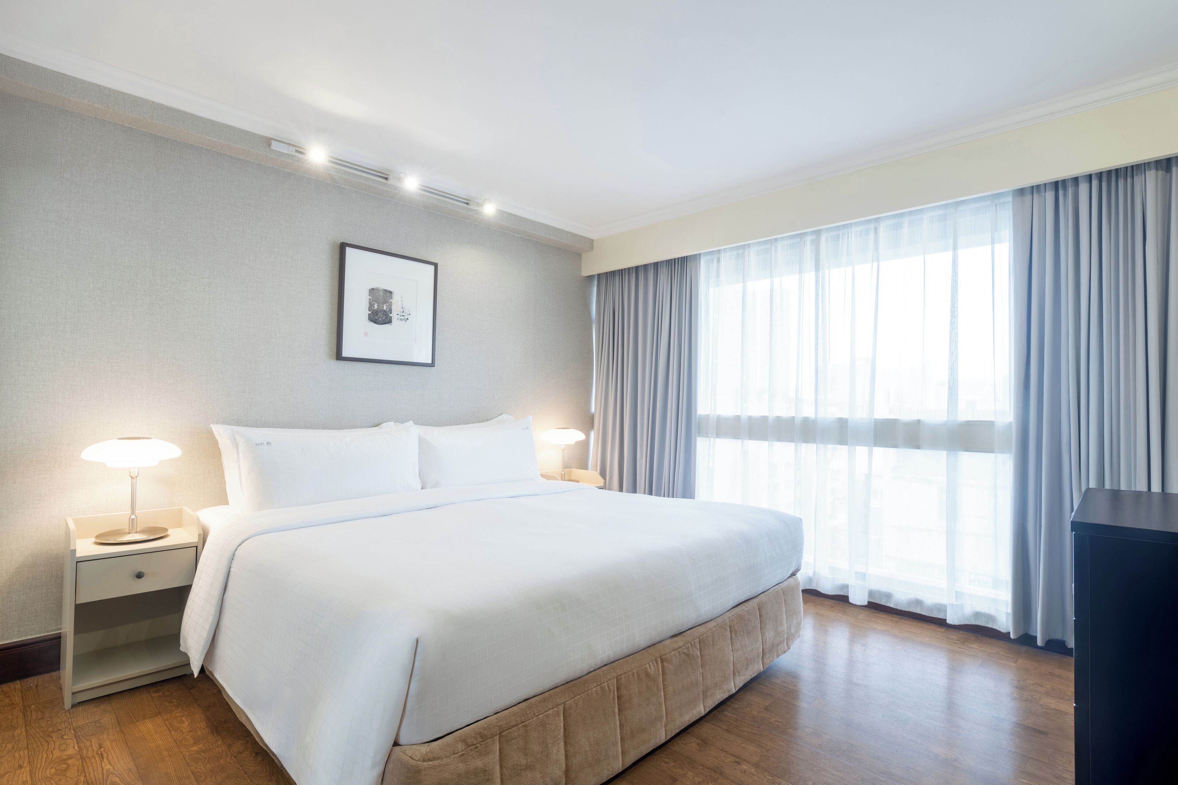 A hotel room with a large bed, bedside lamps, a framed picture on the wall, and a window with curtains.