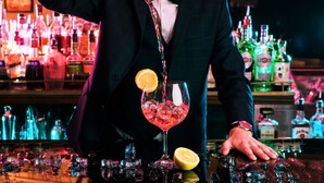 Un barman verse une boisson dans un verre rempli de glaçons et garni d’une tranche de citron.