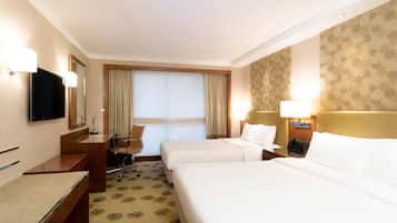 A hotel room with two beds, a desk, a chair, a TV, and a large window with curtains.