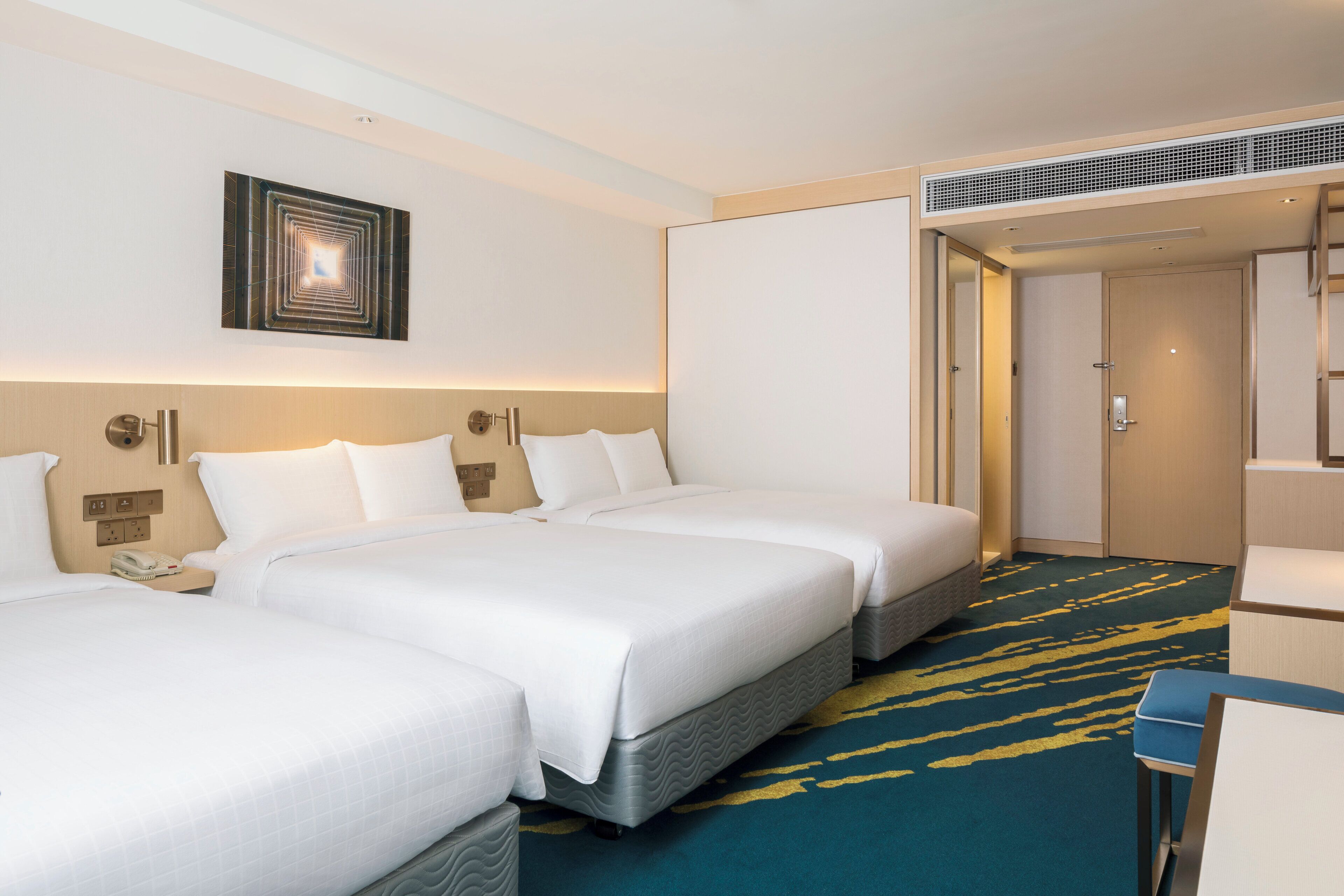 A hotel room with two beds, a desk, a chair, a wall-mounted light, and a door.