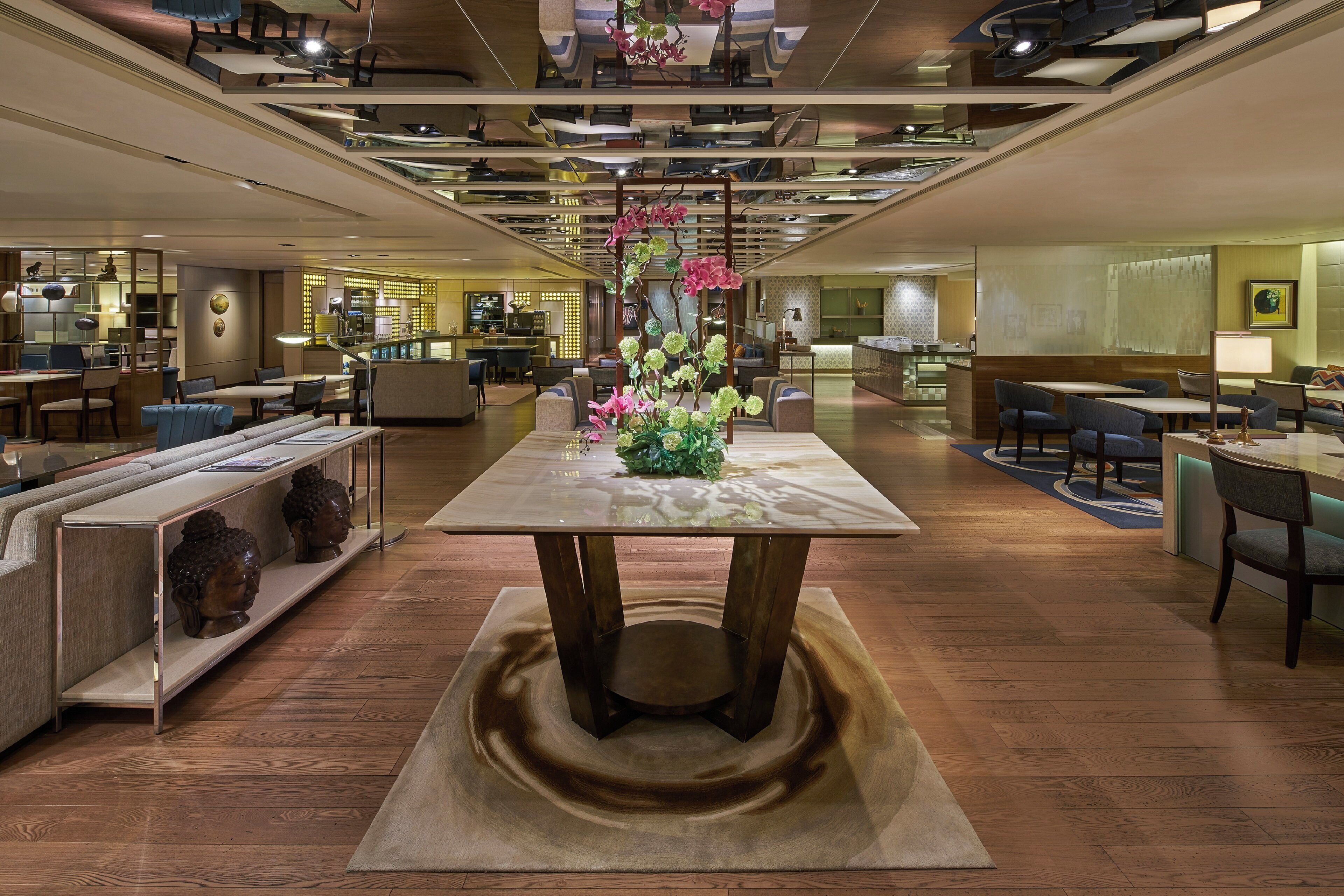 Un hall d'hôtel moderne avec une table centrale, des coins salon et une cuisine en arrière-plan.