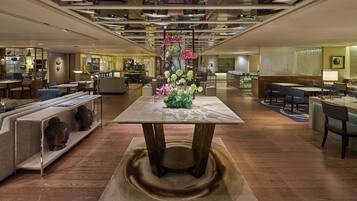 Un hall d'hôtel moderne avec une table centrale, des coins salon et une cuisine en arrière-plan.