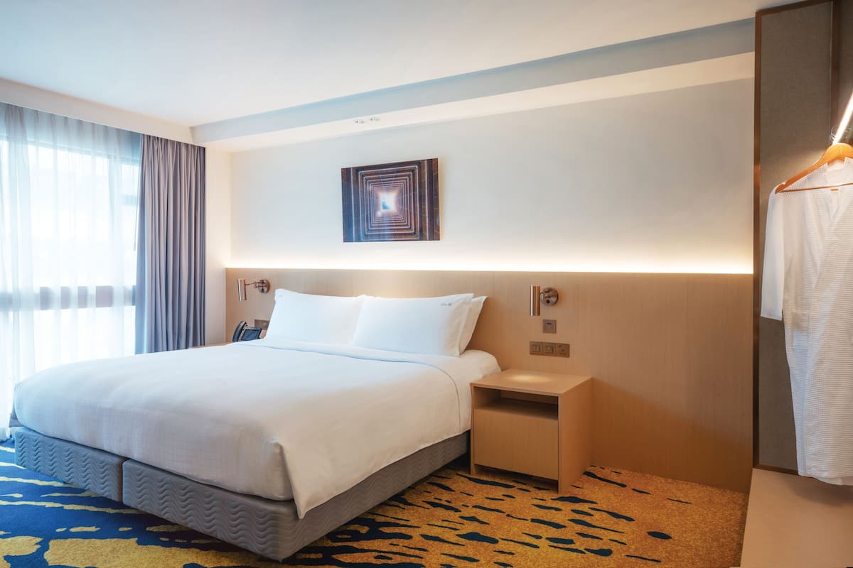A hotel room with a large bed, bedside tables, a hanging towel rack, and a wall-mounted artwork.