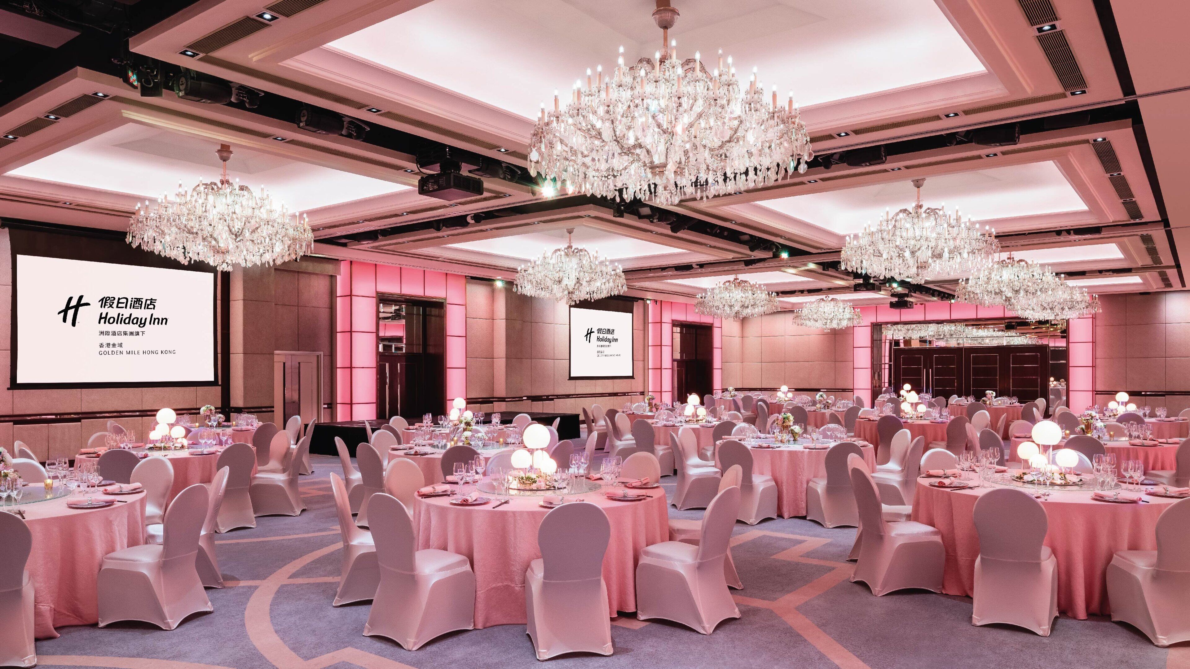 Une salle de banquet avec des tables rondes, des nappes roses et des chaises blanches.