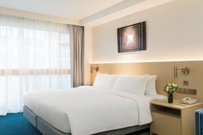 A hotel room with a large bed, a bedside table with a phone and a vase of flowers, and a wall-mounted artwork. - Holiday Inn Golden Mile Hong Kong by IHG (Kowloon)