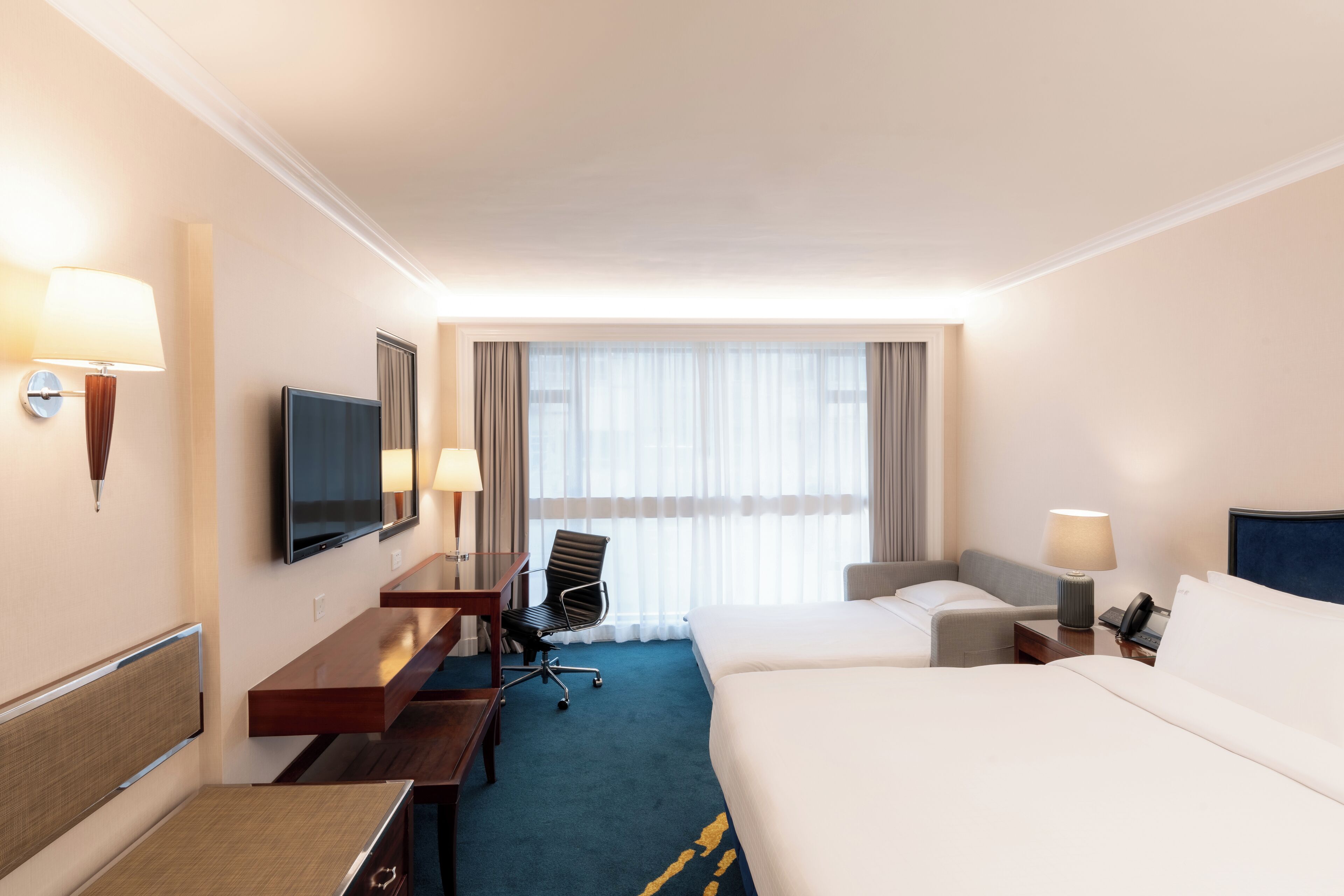 Une chambre d’hôtel avec un lit, un bureau et une chaise, une télévision et une fenêtre avec des rideaux.