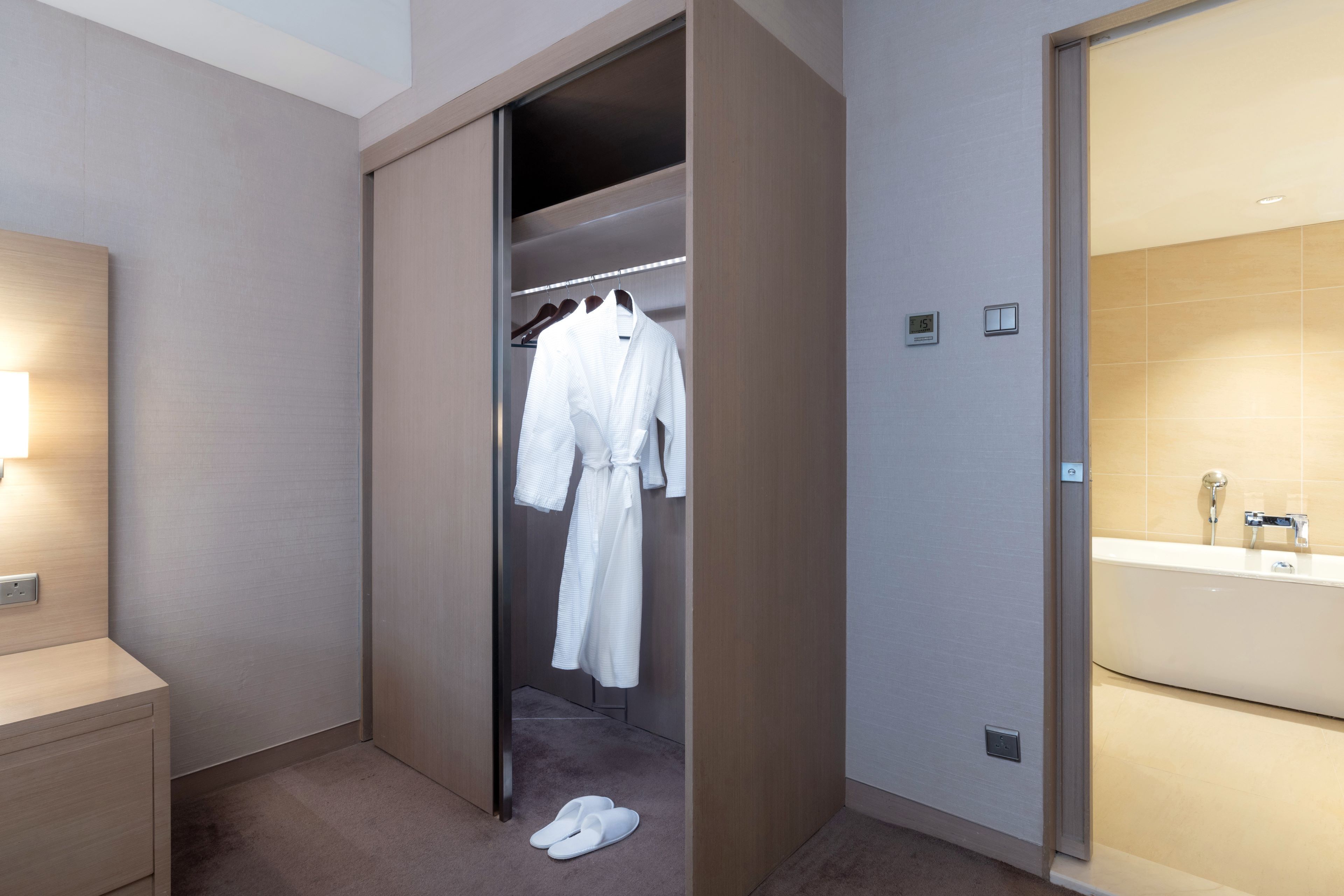 Quarto de hotel com closet espaçoso, banheiro com banheira grande e um par de chinelos no chão.