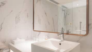 A modern bathroom with a large mirror, a white sink, and marble walls.