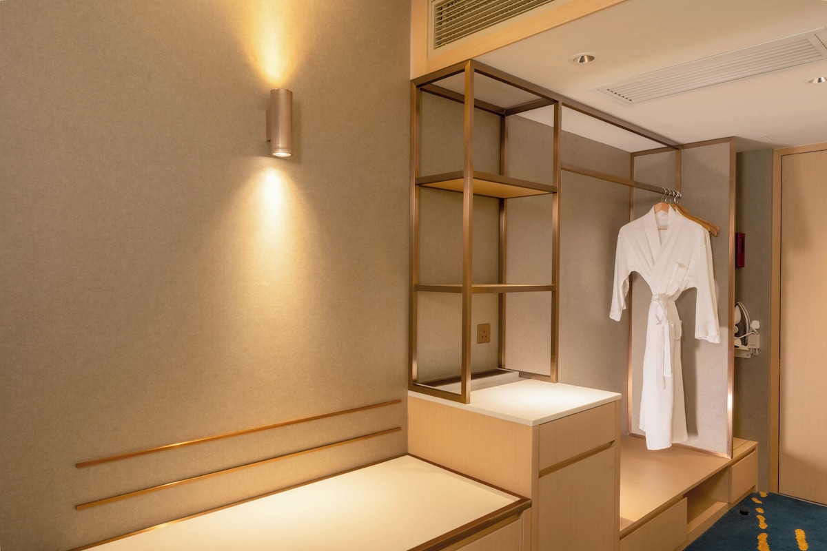 A hotel room with a mirrored wardrobe, a robe hanging inside, and a bedside table.