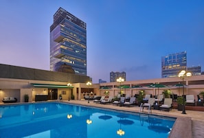 A hotel pool area with lounge chairs and umbrellas, a reception desk, and modern buildings in the background. - Holiday Inn Golden Mile Hong Kong by IHG (Kowloon)