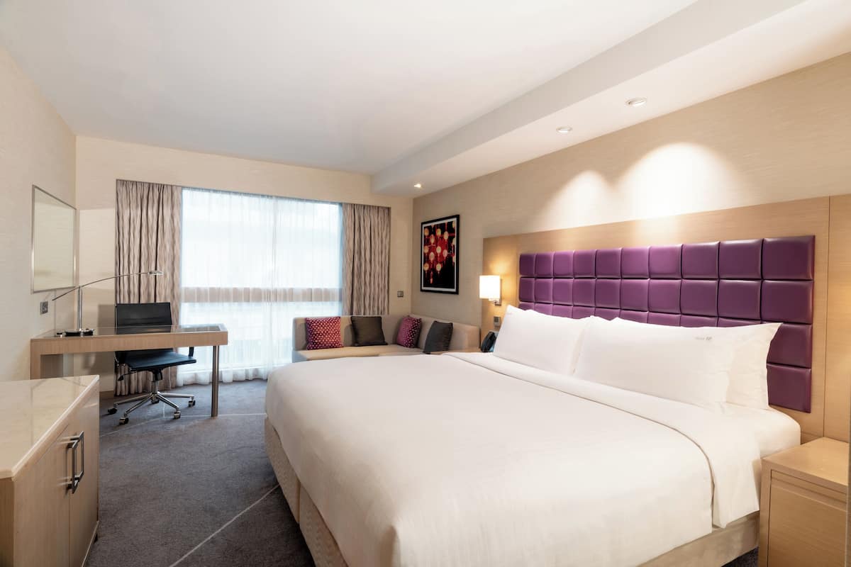 A hotel room with a large bed, a desk with a chair, a computer, and a window with curtains.