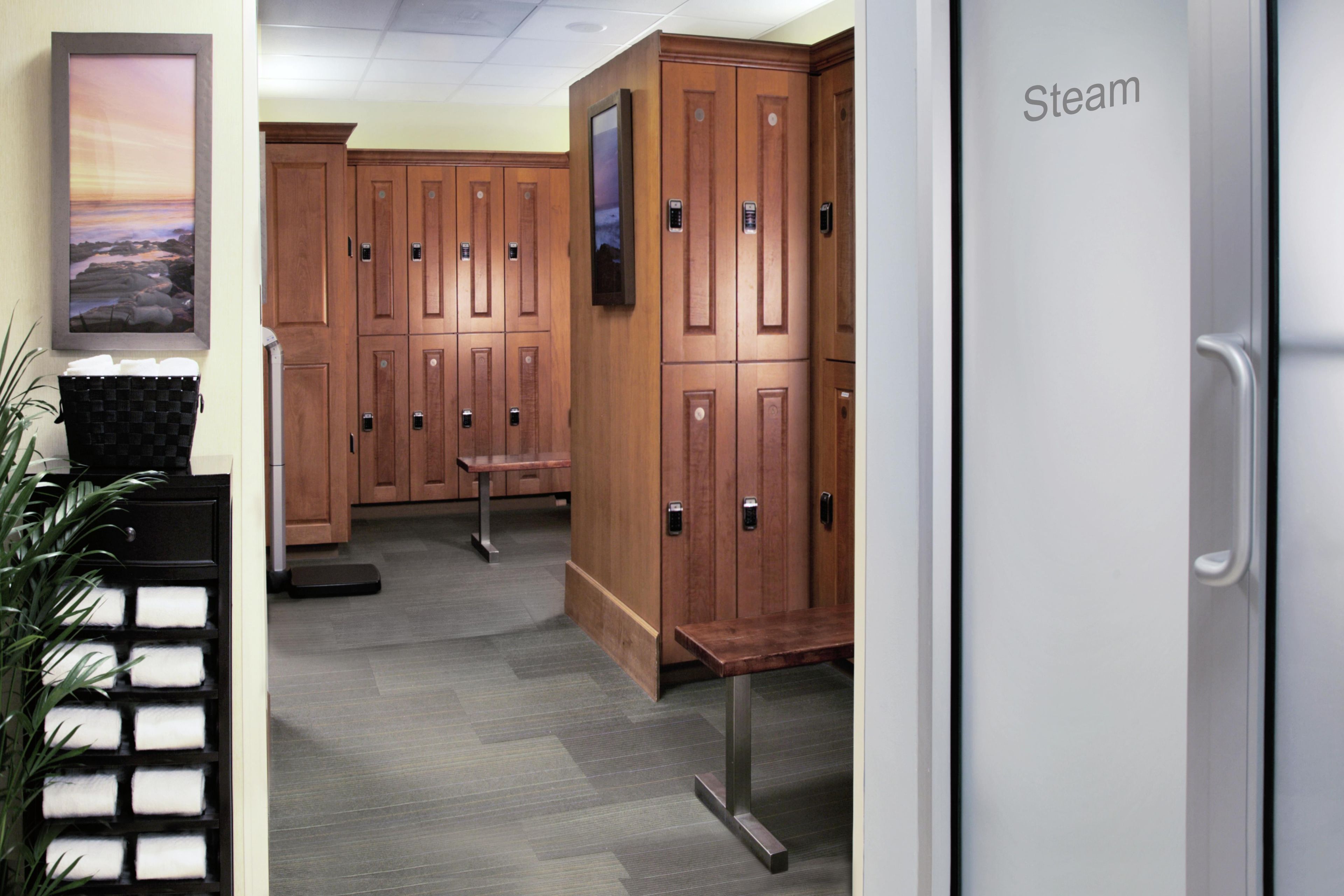 A hotel lobby with wooden lockers, a bench, a scale, and a framed picture on the wall.