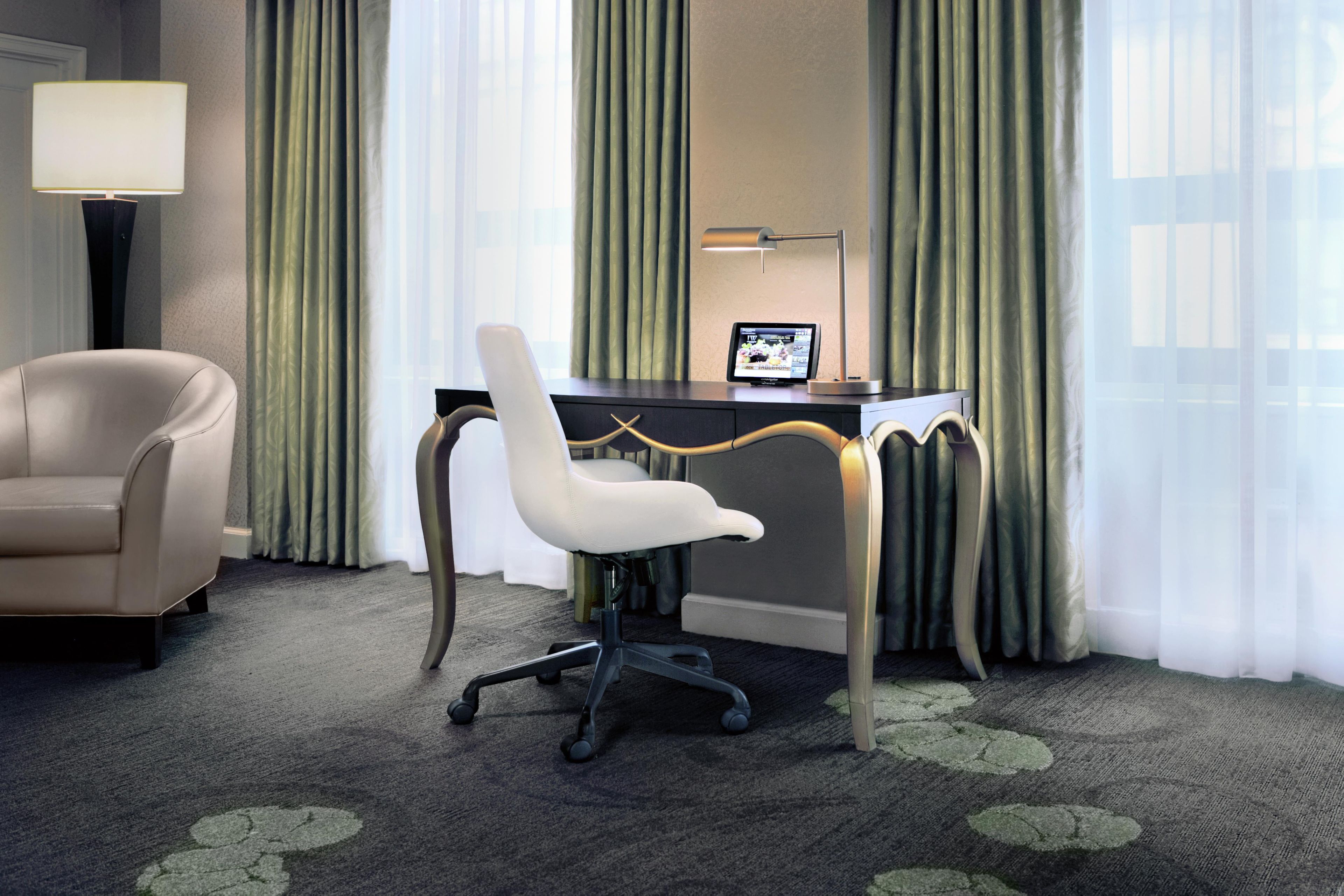 Ett hotellrum med ett skrivbord, en stol, en lampa och en tv.