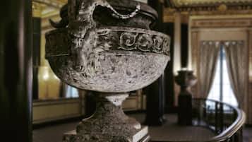 Un recipiente metálico grande y ornamentado con diseños intrincados, ubicado sobre un pedestal en una habitación de arquitectura clásica.