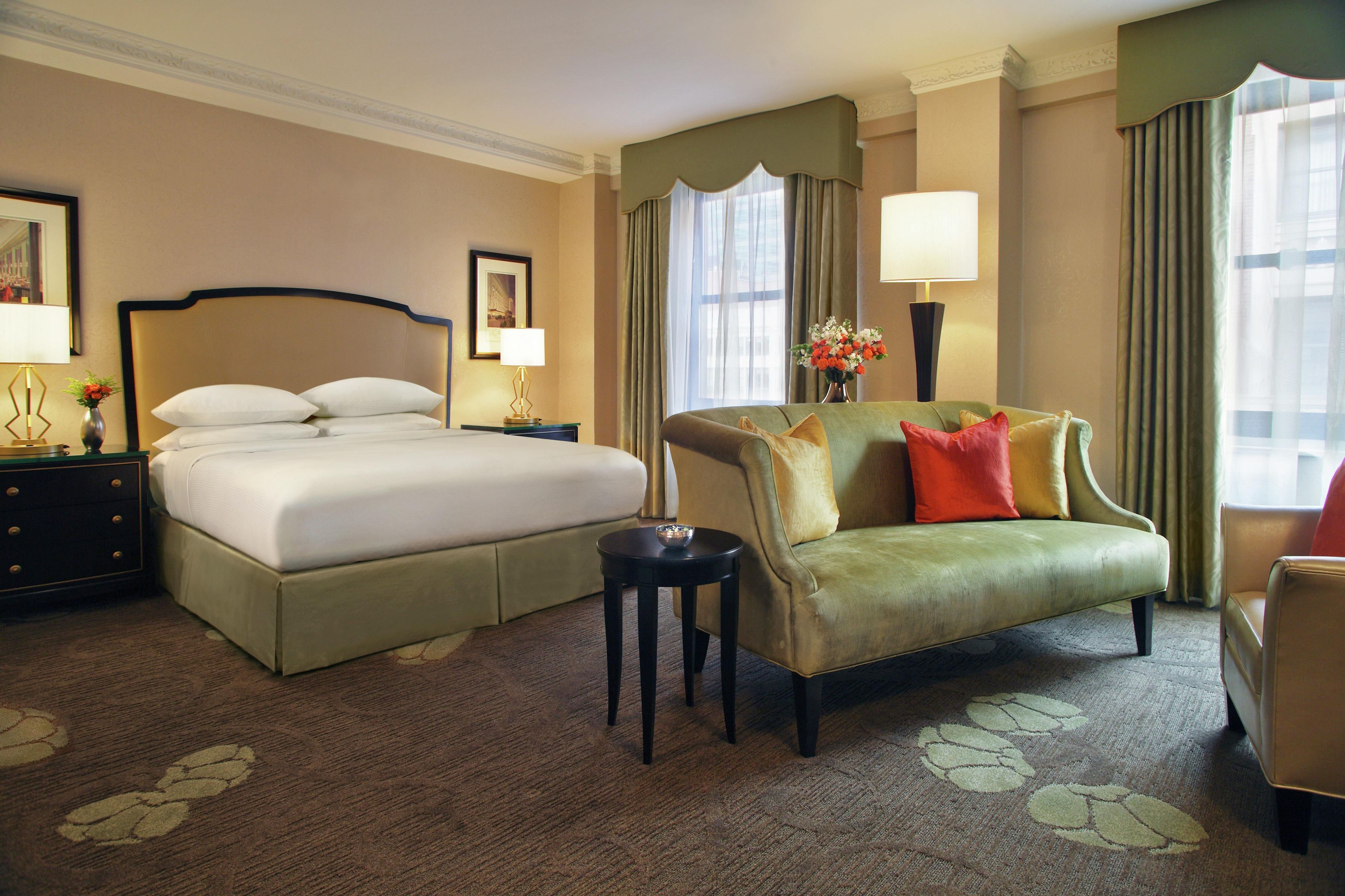 Una habitación de hotel con una cama grande, un sofá, una mesita y una lámpara.