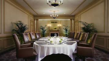 Un comedor formal con una mesa redonda dispuesta para ocho personas, rodeada de sillas de cuero, una araña y plantas en macetas.