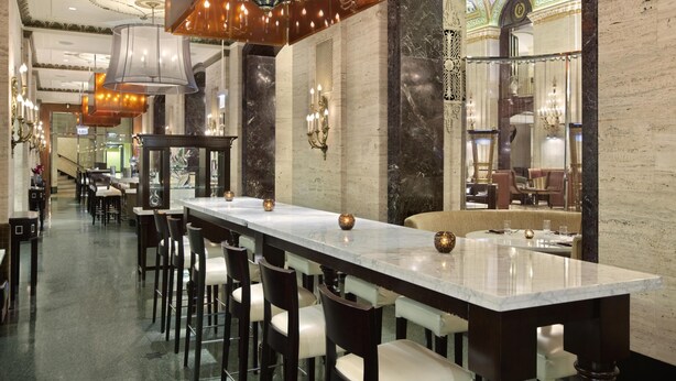 A long dining table with chairs, overhead lighting, and a marble wall with a decorative ceiling. - Palmer House a Hilton Hotel (Chicago)