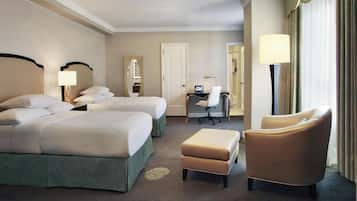 A hotel room with two beds, a desk, a chair, and a lamp.