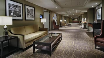 Eine Hotelhalle mit einer Couch, einem Couchtisch, Lampen, gerahmten Bildern an der Wand und einem gemusterten Teppich.