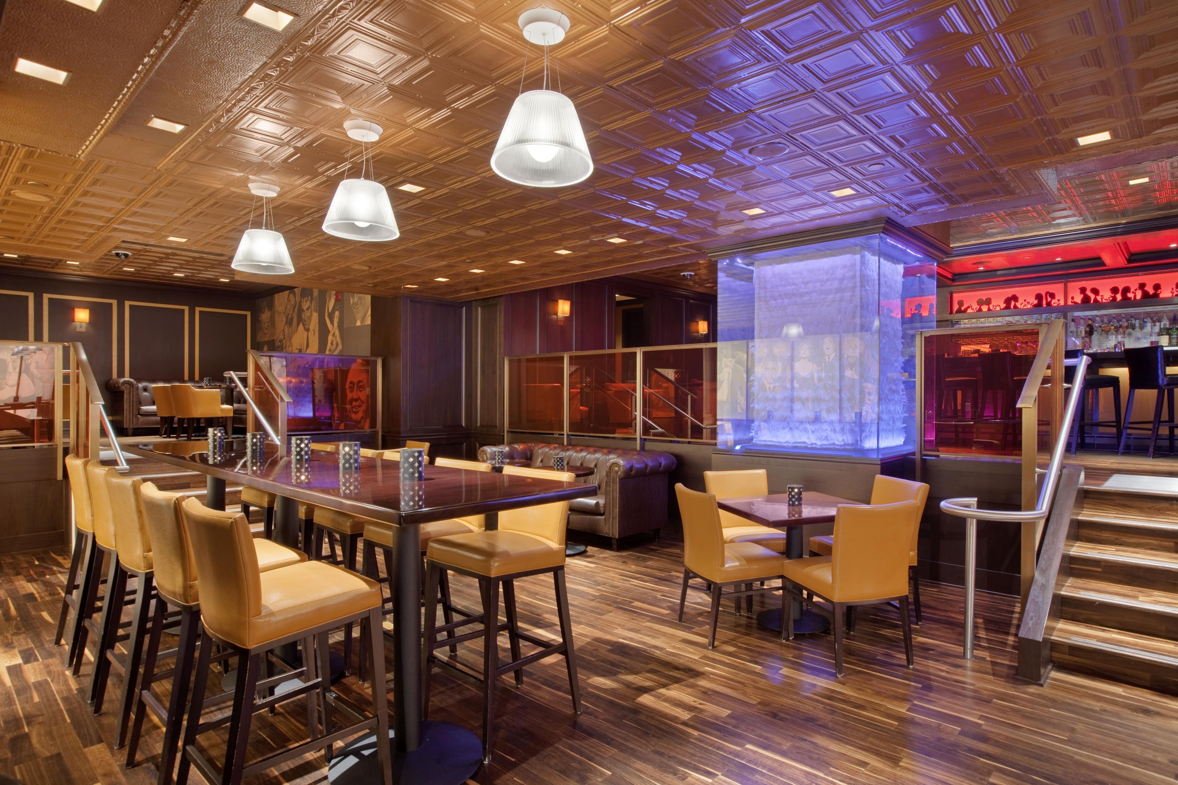 Una zona de bar con suelo de madera, taburetes y lámparas colgantes.